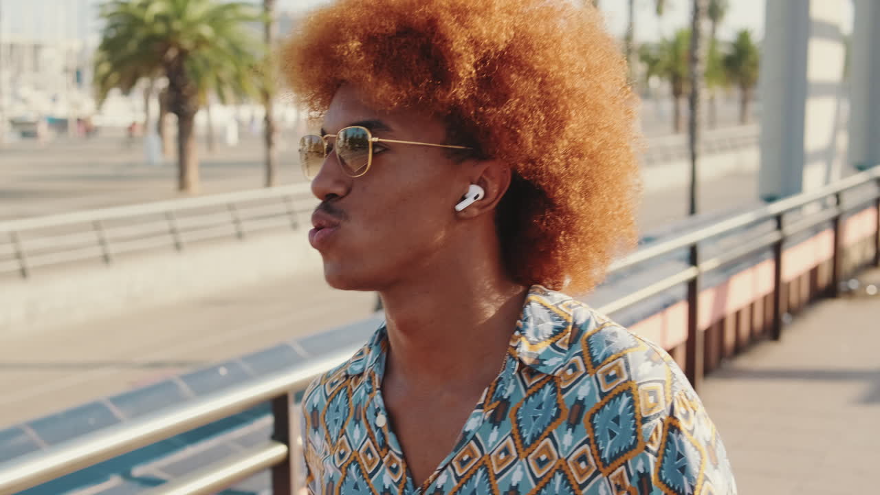 Young Man with Afro Hair and Sunglasses Talking on Wireless Earbuds