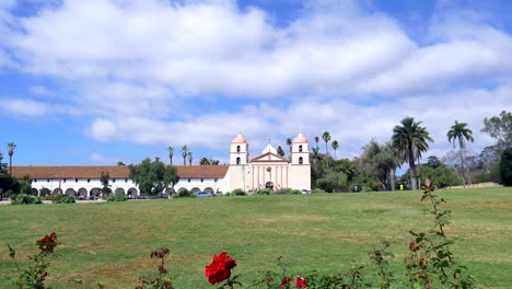 reveal shot of the picturesque santa barbara mission building from behind bright red roses in california