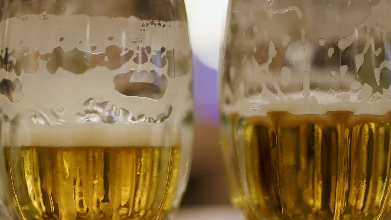 Hand rotates half-full beer glass on bar counter, warm ambient lighting, shallow focus