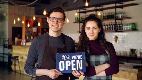 cheerful attractive people coffee-house owners are holding "we are open" sign while standing inside coffee shop. opening new business and people concept.