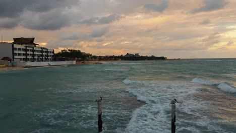 Fliegen-Sie-Tief-über-Das-Türkisblaue-Wasser-Der-Karibik,-Um-Die-Hotels-Und-Den-Strand-Von-Playa-Paraiso-Beach-In-Tulum-Mexiko-An-Einem-Bewölkten-Tag-Mit-Einem-Goldenen-Sonnenuntergangshimmel-Zu-Enthüllen