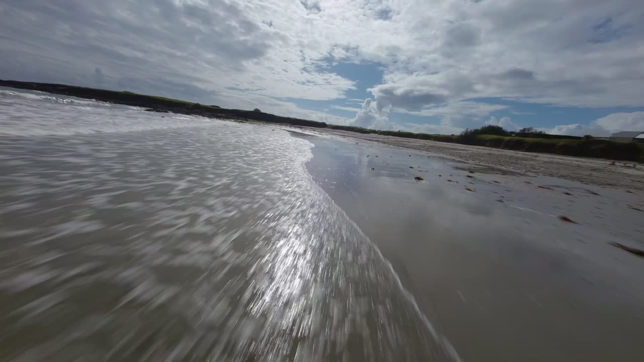 FPV drone skim over reflective shallow water at Kersidan Beach, Brittany, during low tide with dramatic light reflecting off water surface