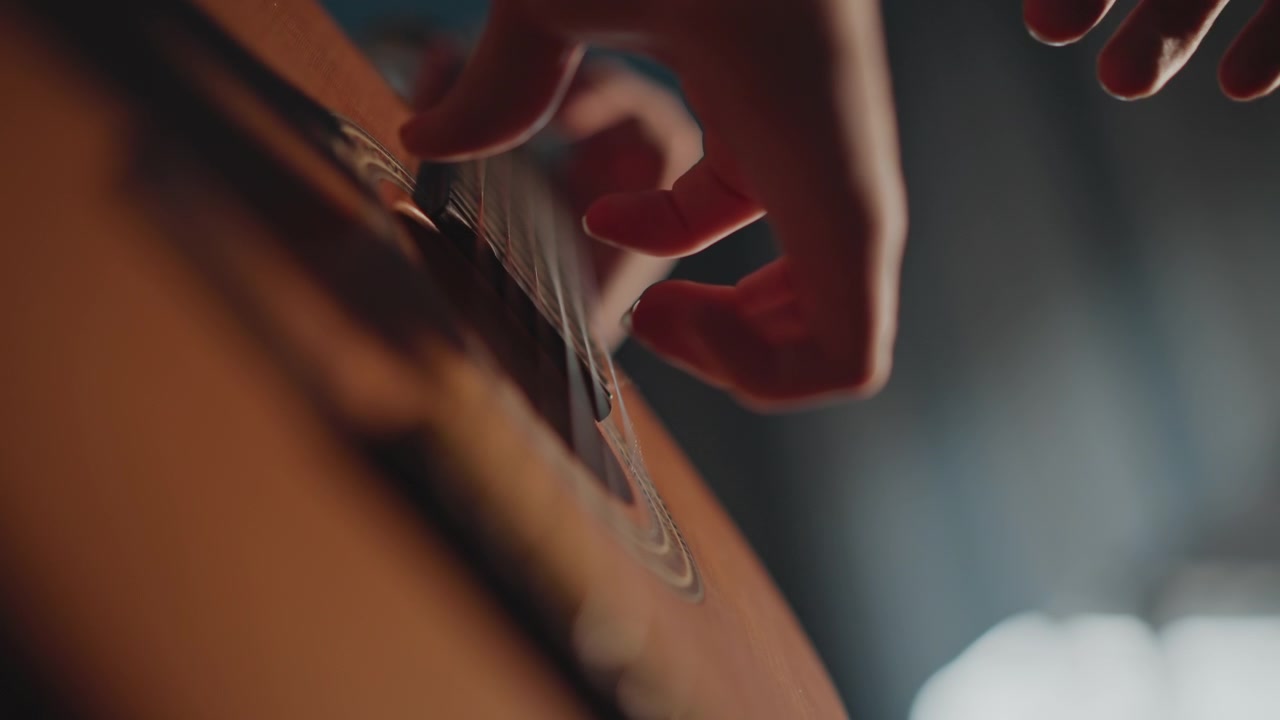 Nærbillede af fingre, der plukker strenge på en akustisk guitar i varmt studielys, hvor en begynderstuderende øver fingerstyle-teknik med en tålmodig coach, med fokus på detaljerede nylonstrenge, højrehåndsbevægelse og en blød, stemningsfuld atmosfære