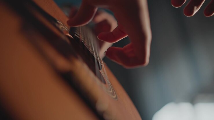 Closeup acoustic guitar fingers plucking strings in warm studio light, beginner student practices fingerstyle technique with patient coach, detailed nylon strings, right hand motion, soft ambient mood