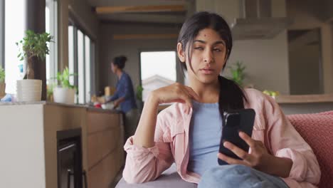 Video-of-thoughtful-biracial-woman-sitting-on-sofa-and-using-smartphone