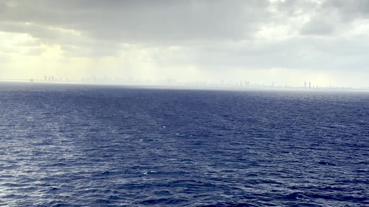 Storm clouds hang over the Atlantic Ocean with the Miami skyline faintly visible on the horizon.
