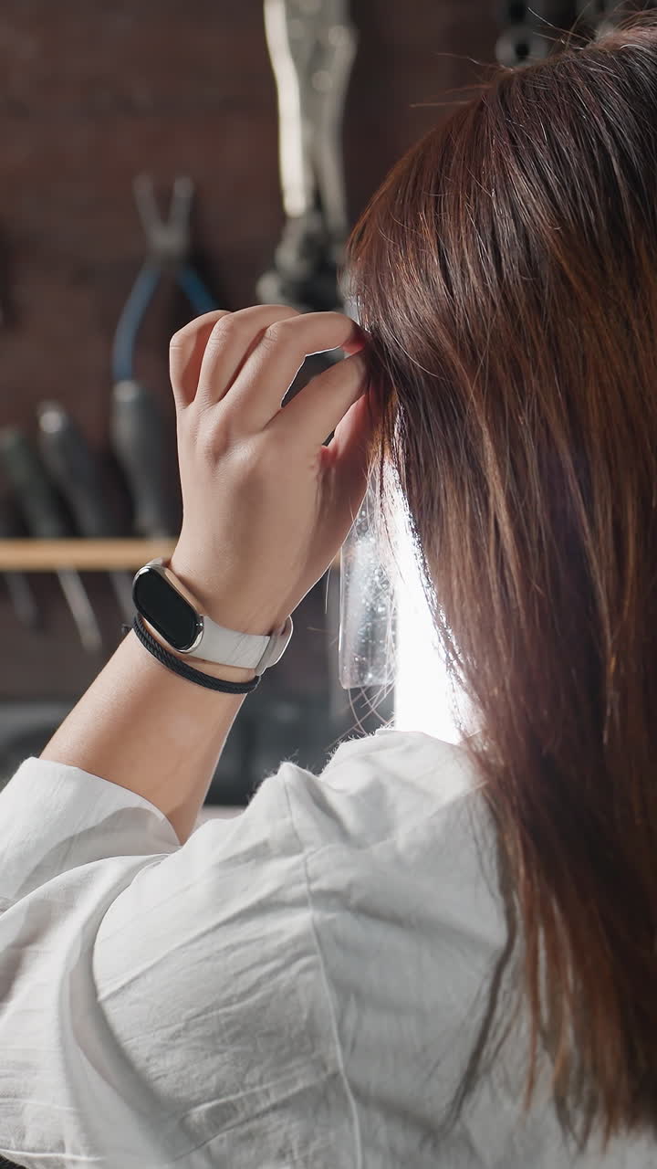 색 코트를 입은 학생이 보호 얼굴 방패를 들고, 그것을 입고, 좌석에 다시 휴식을 취하고, 왼손에 스마트 시계와 검은 팔를 달고, 워크 기계 및 장비로 둘러싸여 있습니다.