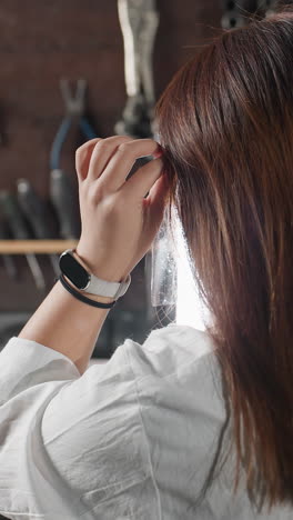 색 코트를 입은 학생이 보호 얼굴 방패를 들고, 그것을 입고, 좌석에 다시 휴식을 취하고, 왼손에 스마트 시계와 검은 팔를 달고, 워크 기계 및 장비로 둘러싸여 있습니다.