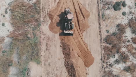 aerial top down view of earth mover flattening material on ground in pakistan