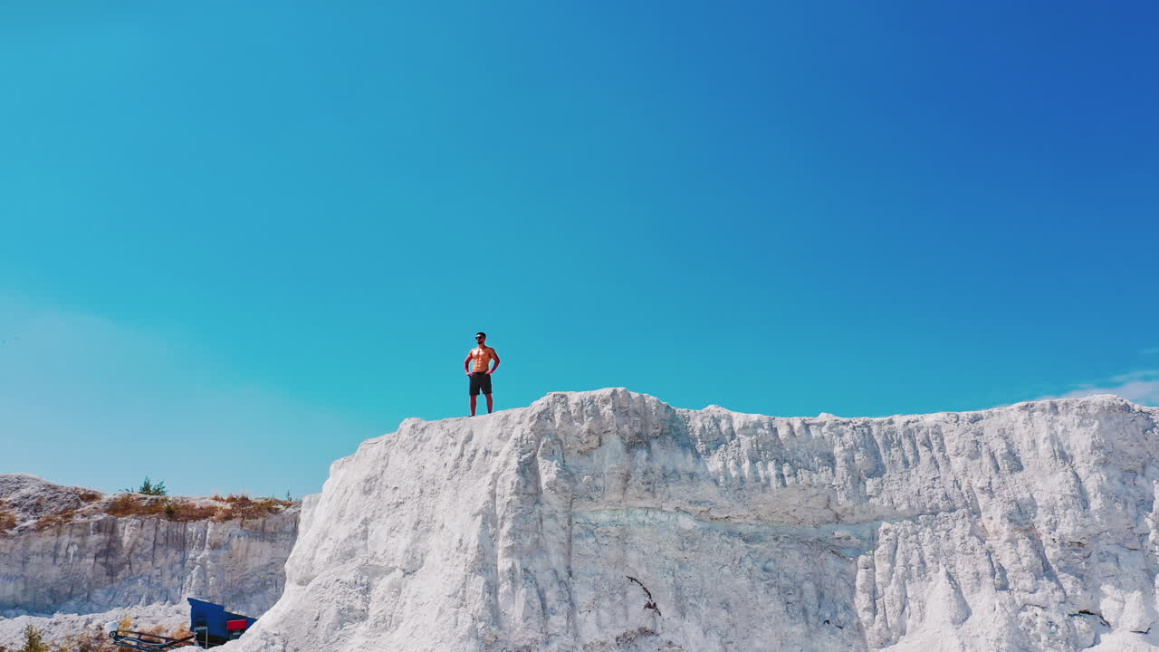 Drone view on a sportive man standing on the edge of the mountain. Shirtless athlete on the top of white canyon under clear sky in summer day.
