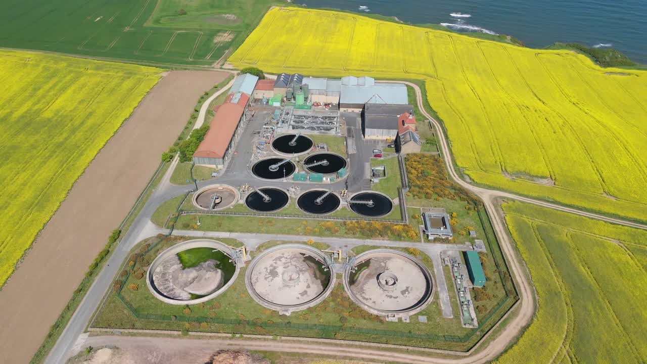 Aerial drone view of a wastewater treatment plant in a bright yellow rapeseed field on a sunny summer day in North Yorkshire, UK