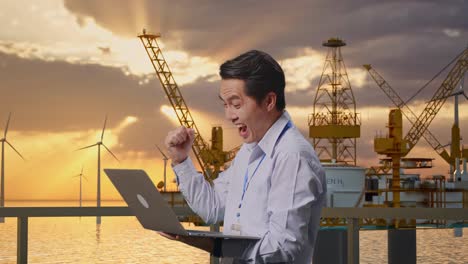 engineer celebrating success with laptop at oil rig and wind turbines