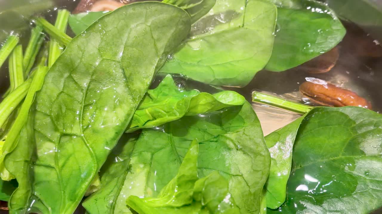 Primo piano dall'alto di foglie di spinaci freschi che cuociono nel brodo bollente e fumante della zuppa.