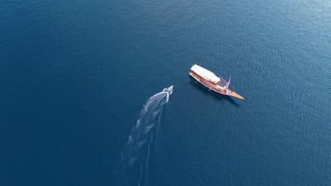 high aerial of a speedboat heading towards a large anchored boat over dark blue ocean