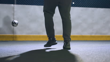 leg view of man kicking soccer ball against wall under bright stadium lighting at night, focus on athletic motion and shadow with urban environment and illuminated background