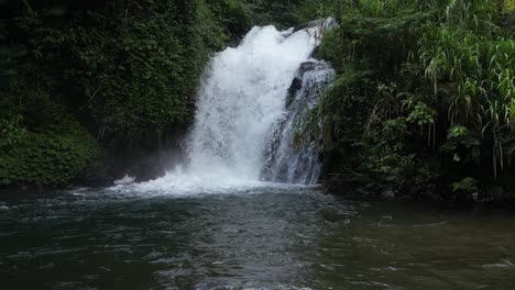 a small, hidden waterfall in the depths of balinese jungle on a sunny afternoon, aerial