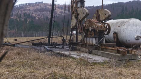 old and rusty oil drilling equipment with storage tank in a field with mountains in the distance