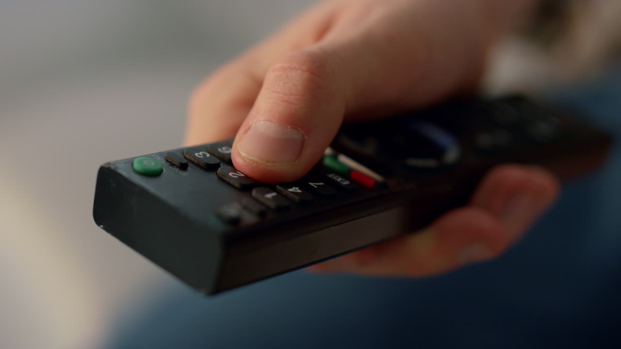 손가락이 리모컨 버튼을 누르고 클로즈업 알려지지 않은 남자가 채널을 바꾸고 있습니다.
