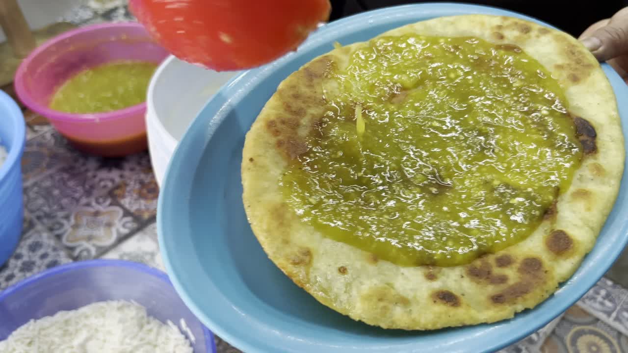 Hand dipping a freshly cooked huarache into a bucket of creamy sauce at a Mexican street food stand