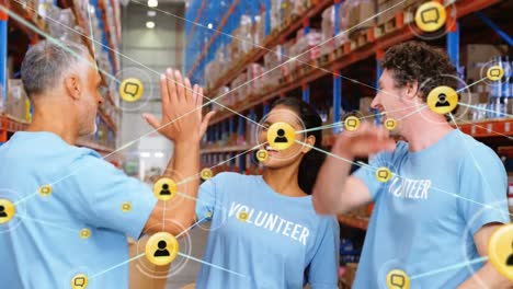 animation of network of people icons over diverse volunteer group high fiving at storage warehouse