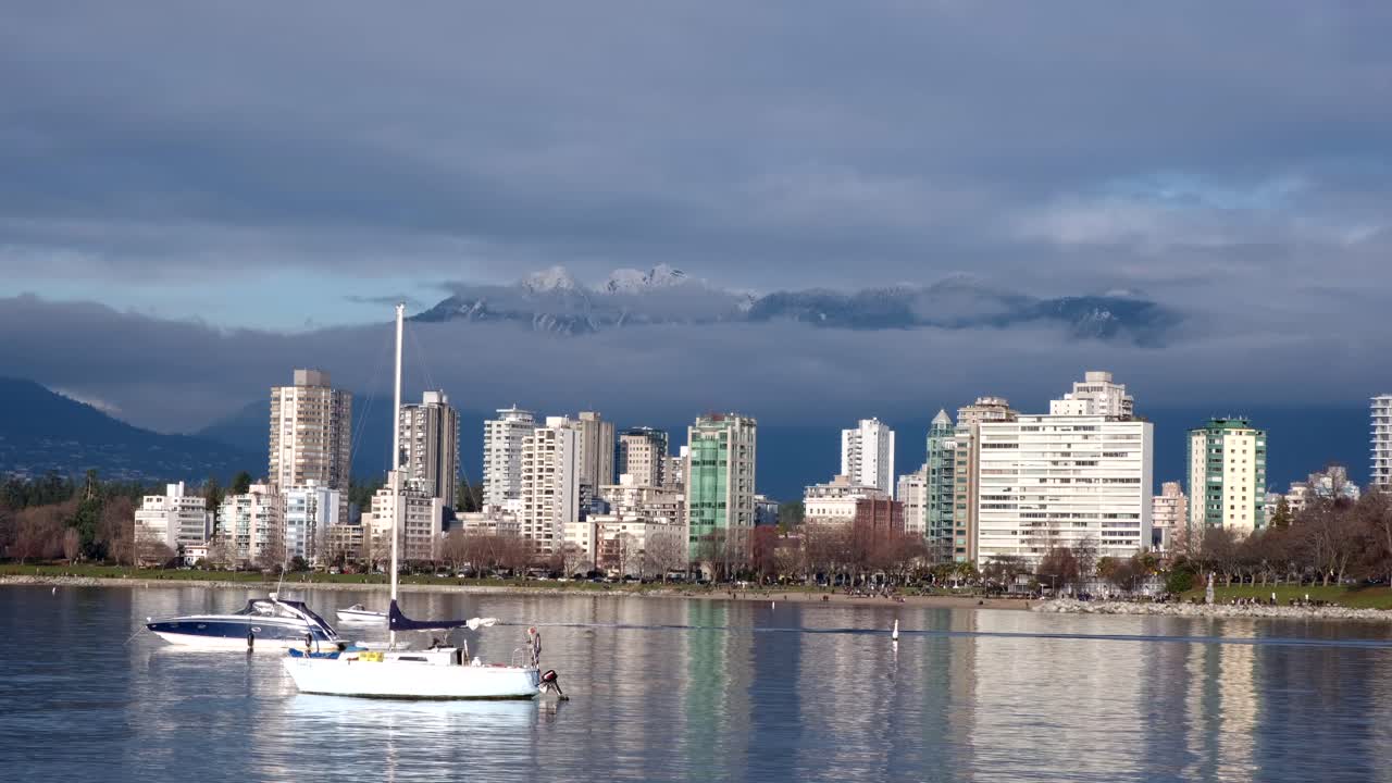 pequeño bote cruzando el marco con otros dos botes anclados en la bahía inglesa cerca del centro de vancouver en un soleado día de invierno con picos nevados y nubes en el fondo