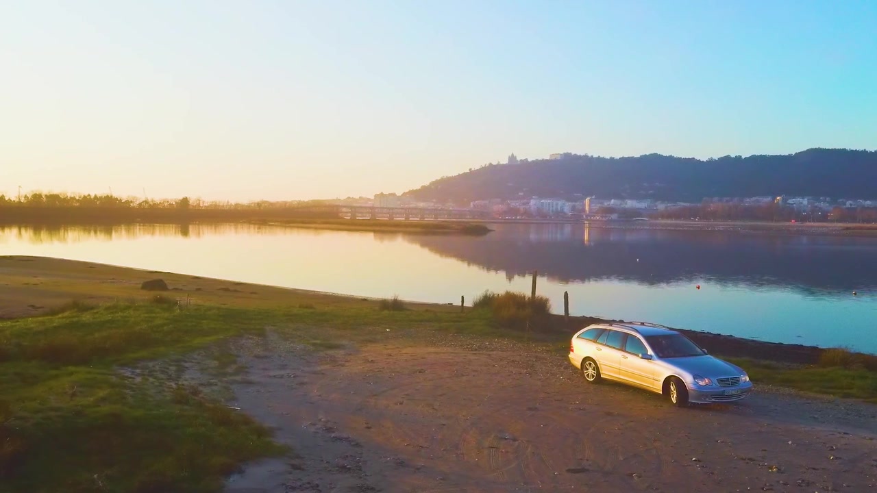 Ripresa con drone di una Mercedes C220 - Rotazione accanto al fiume e al paesaggio urbano durante l'ora d'oro