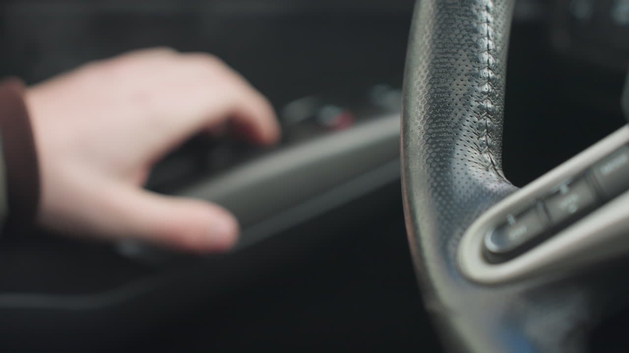 fair skinned hand sliding from center console to steering wheel inside modern car interior close up detailed leather stitching shallow depth of field natural light motion control interaction focus