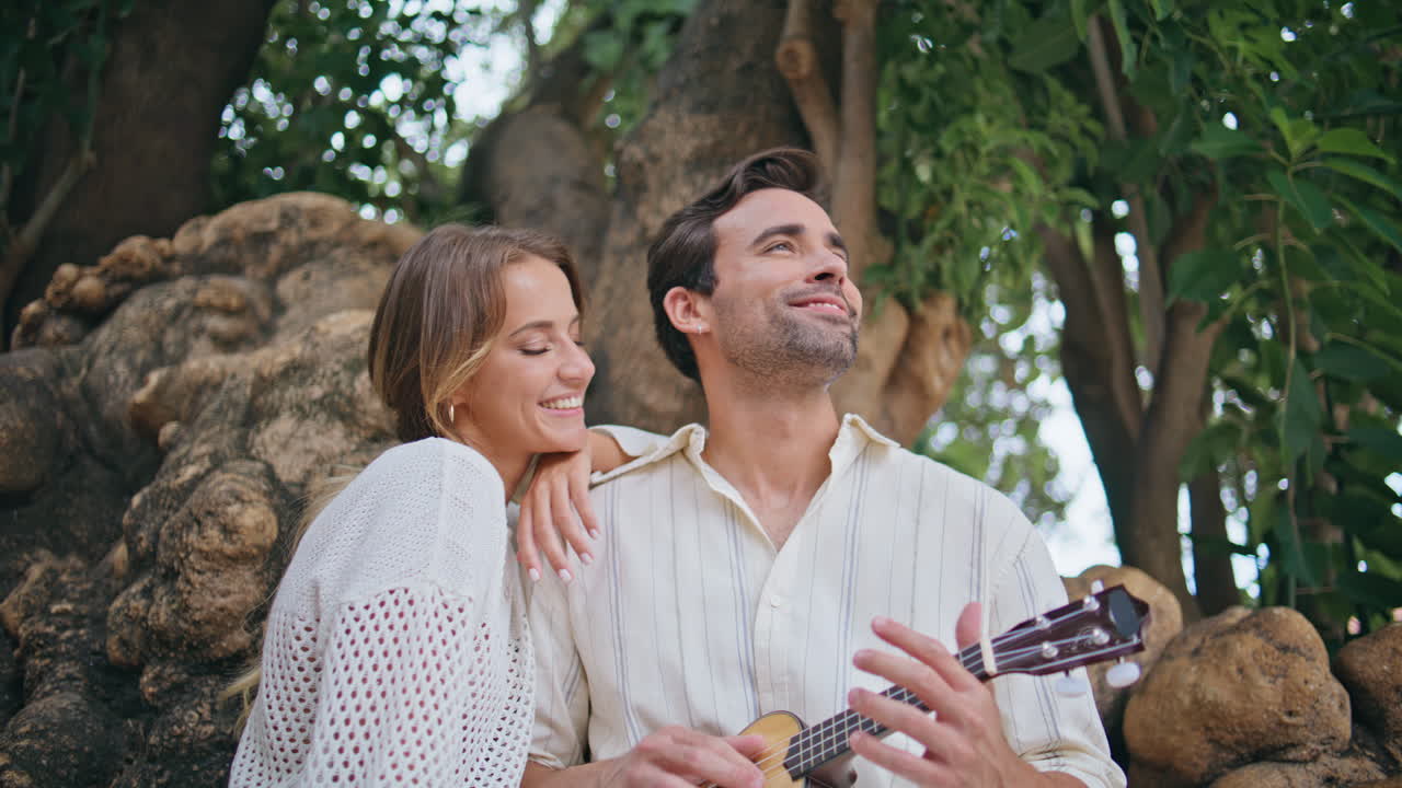 사랑에 빠진 신혼 부부가 공원에서 기타 음악을 즐기고 있습니다. 우쿨레를 연주하는 마초