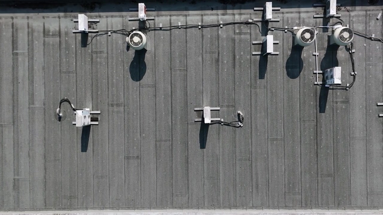 Top-down view of flat rooftop lighting equipment on a dark industrial roof, with cables, mounted fixtures, shadows and technical infrastructure details.