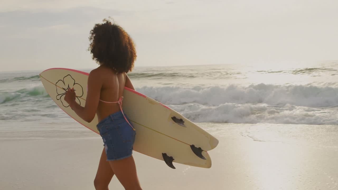 Side view of African American female surfer running with surfboard on the beach 4k