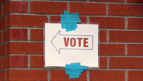 vote here sign with left pointing arrow taped to brick wall