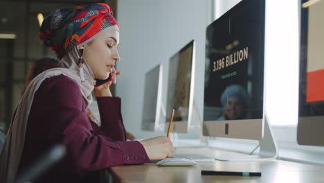 businesswoman in hijab talking on phone and working on computer