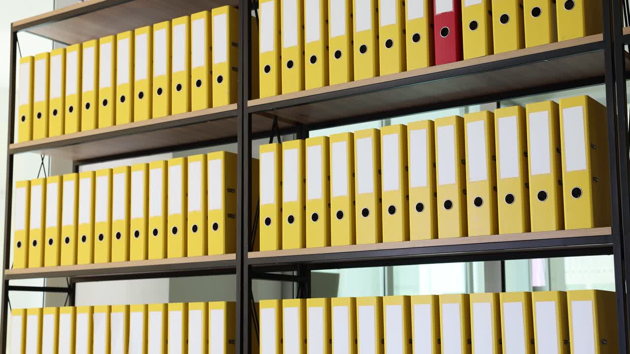 Rows of yellow binders on shelves with a single red binder