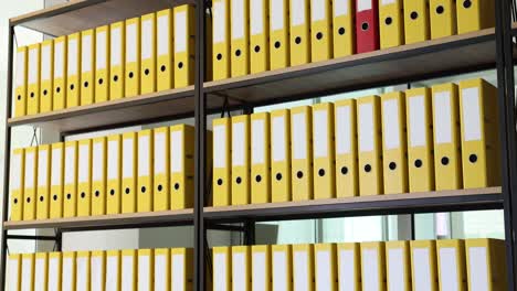 rows of yellow binders on shelves with a single red binder