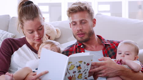 Young-white-couple-reading-book-with-two-toddlers,-close-up