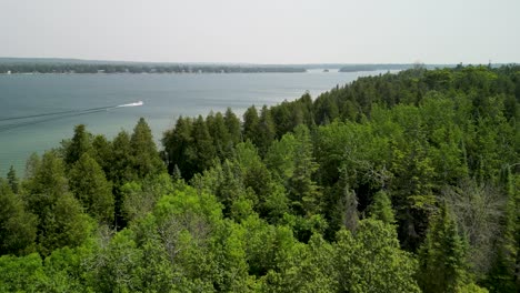 aerial ascent over forested trees reveal of water and boat, lake huron, michigan