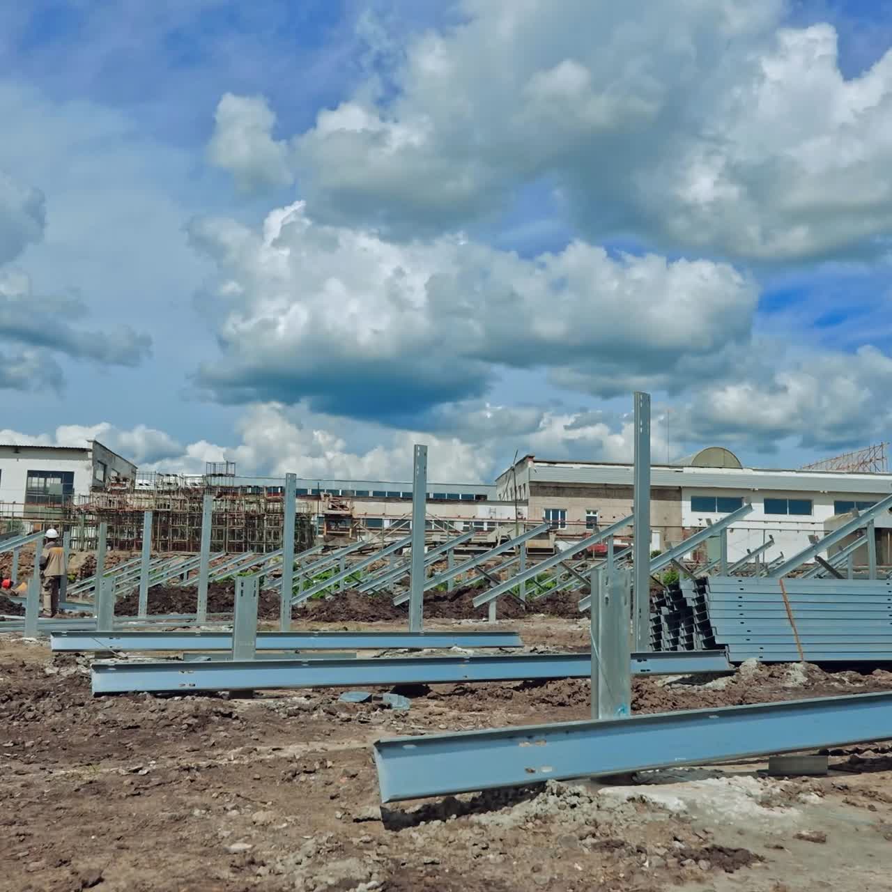 Building of a new solar farm. Teamwork of engineers constructing metal basis for solar panels under cloudy sky. Time lapse.