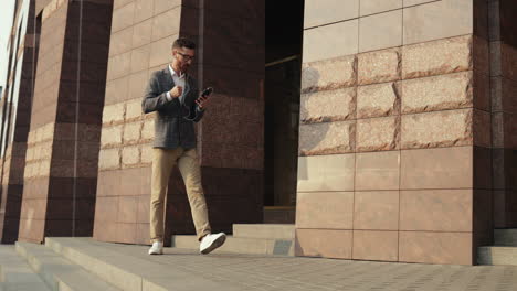 stylish man listening music on the smartphone via earphones while walking and dancing joyfully in the street