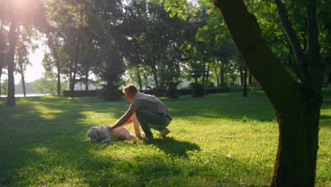 Joyful-happy-man-petting-tired-golden-retriever-lying-on-field-after-training.