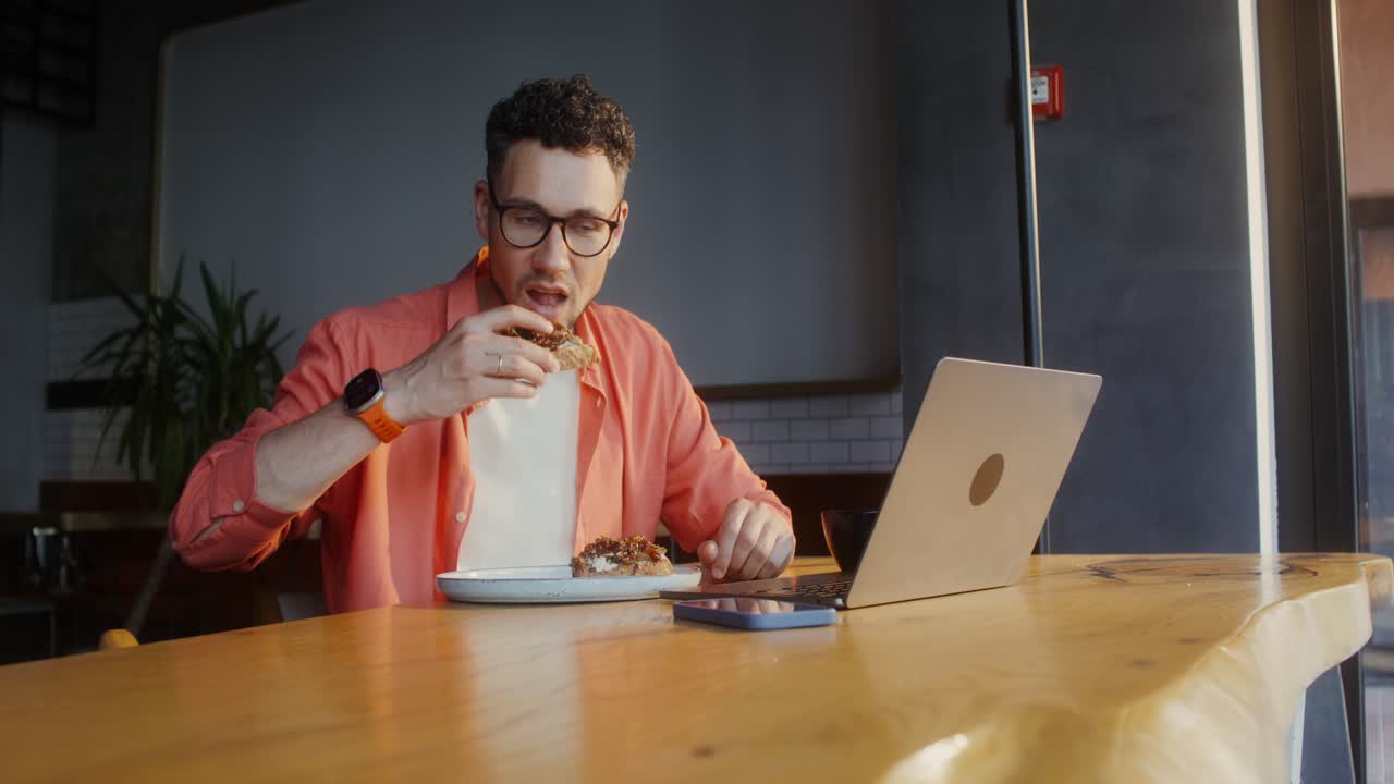 Man eating sandwich and working on laptop in cafe