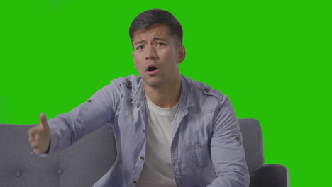 Studio-Shot-Of-Disappointed-Young-Man-Sitting-On-Sofa-Watching-Sport-On-TV-Against-Green-Screen-3