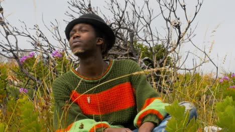 a young trendy african man with braids and a hat relaxes with a smoke in the flowering bush