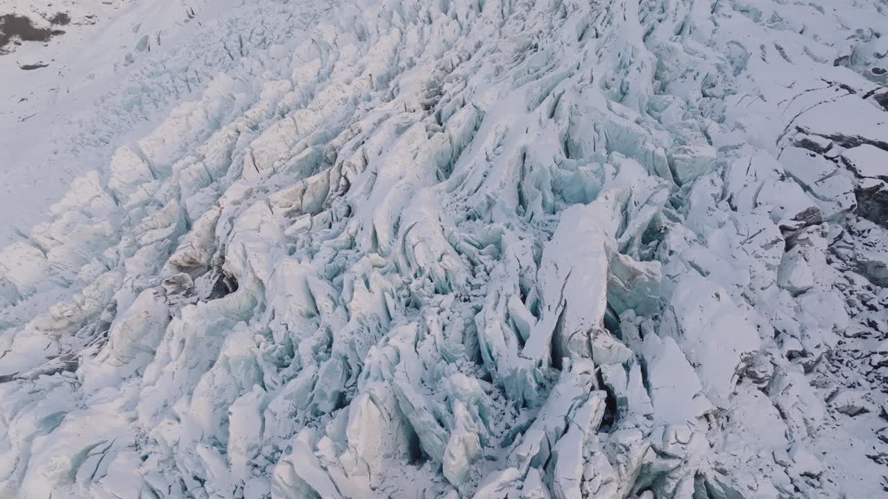 Vista aérea de formaciones de hielo texturizadas en el glaciar Falljokull cubierto de nieve, Islandia, al atardecer.