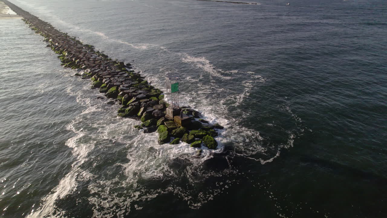 Homem pescando, lançando a linha no oceano de um molhe. Imagem aérea de drone próximo a uma boia de canal sobre as rochas.