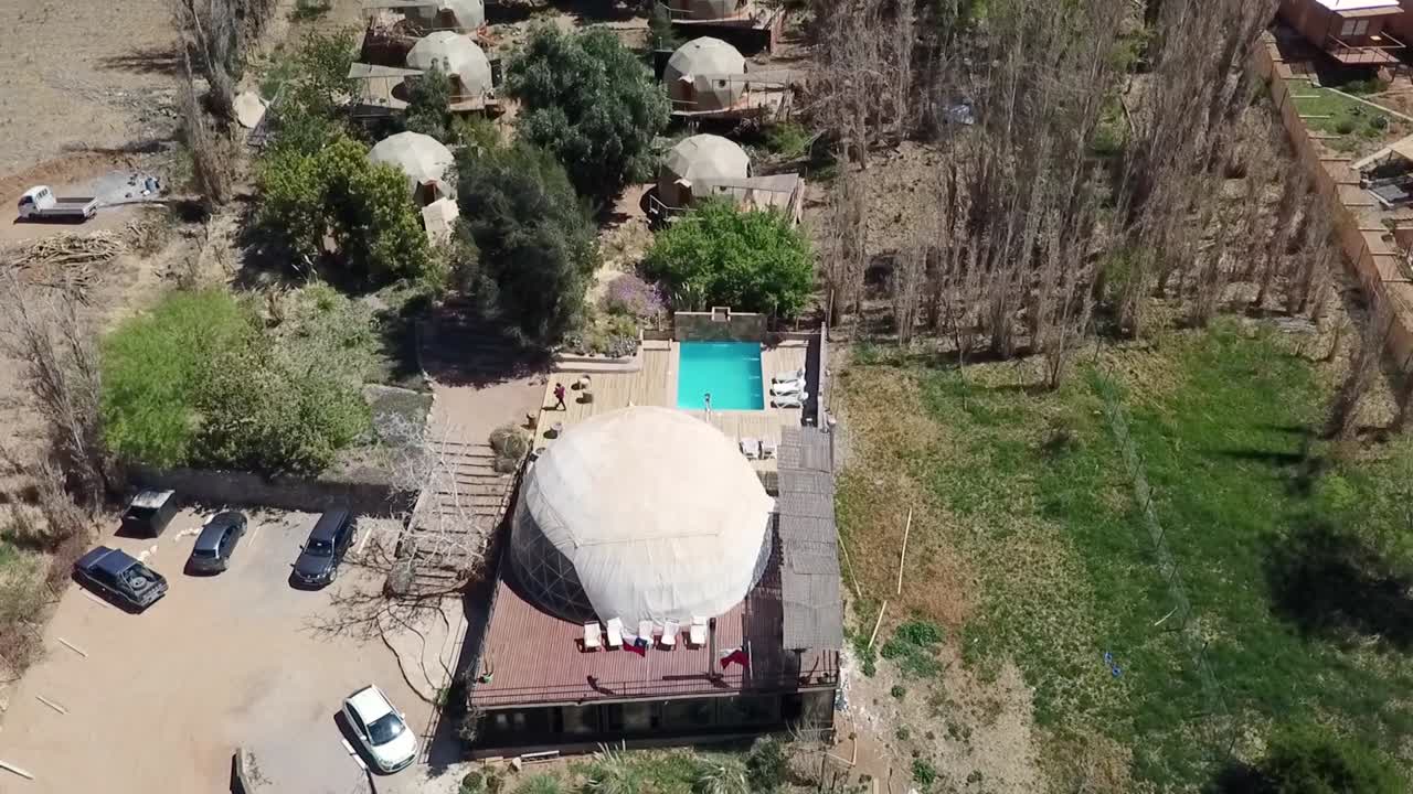 drone volando sobre cúpulas geodésicas en el desierto chileno con piscina