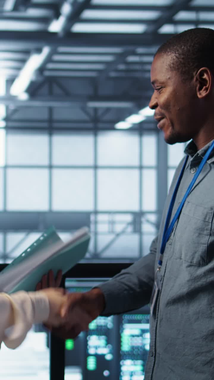 Vertical video Cheerful admins meeting in data center to review reports, doing handshake