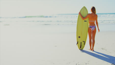 Rückansicht-Einer-Jungen-Kaukasischen-Frau,-Die-Mit-Einem-Surfbrett-Am-Strand-Steht-4k