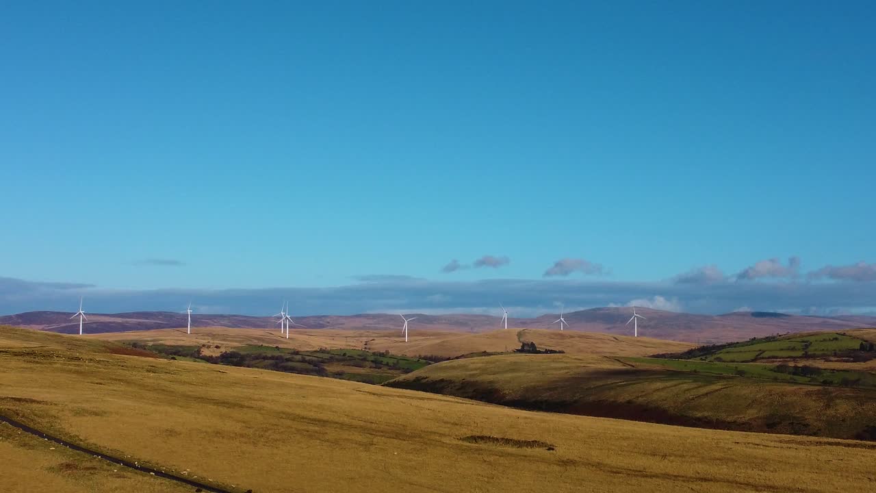 Slow Sideways Drone View Over Wales with Rolling Hills and Valley with Wind Farm in Distance on Natural Landscape. Renewable Energy Technology with Nature Concept