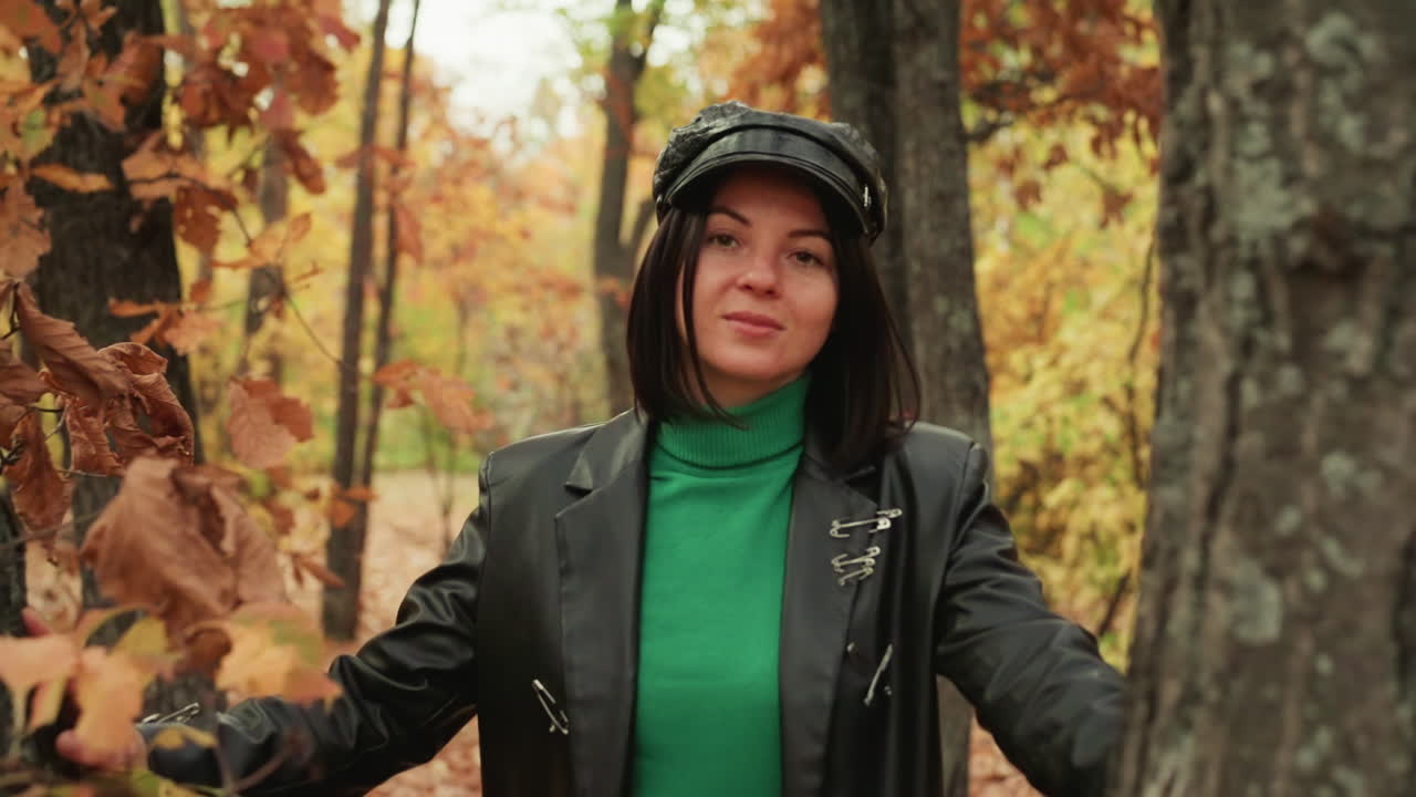 woman in leather jacket amid autumn oaks, confident model explores woodland, green turtleneck and cap, leaves rustle around trunk, candid portrait with rugged vibe and cinematic composition