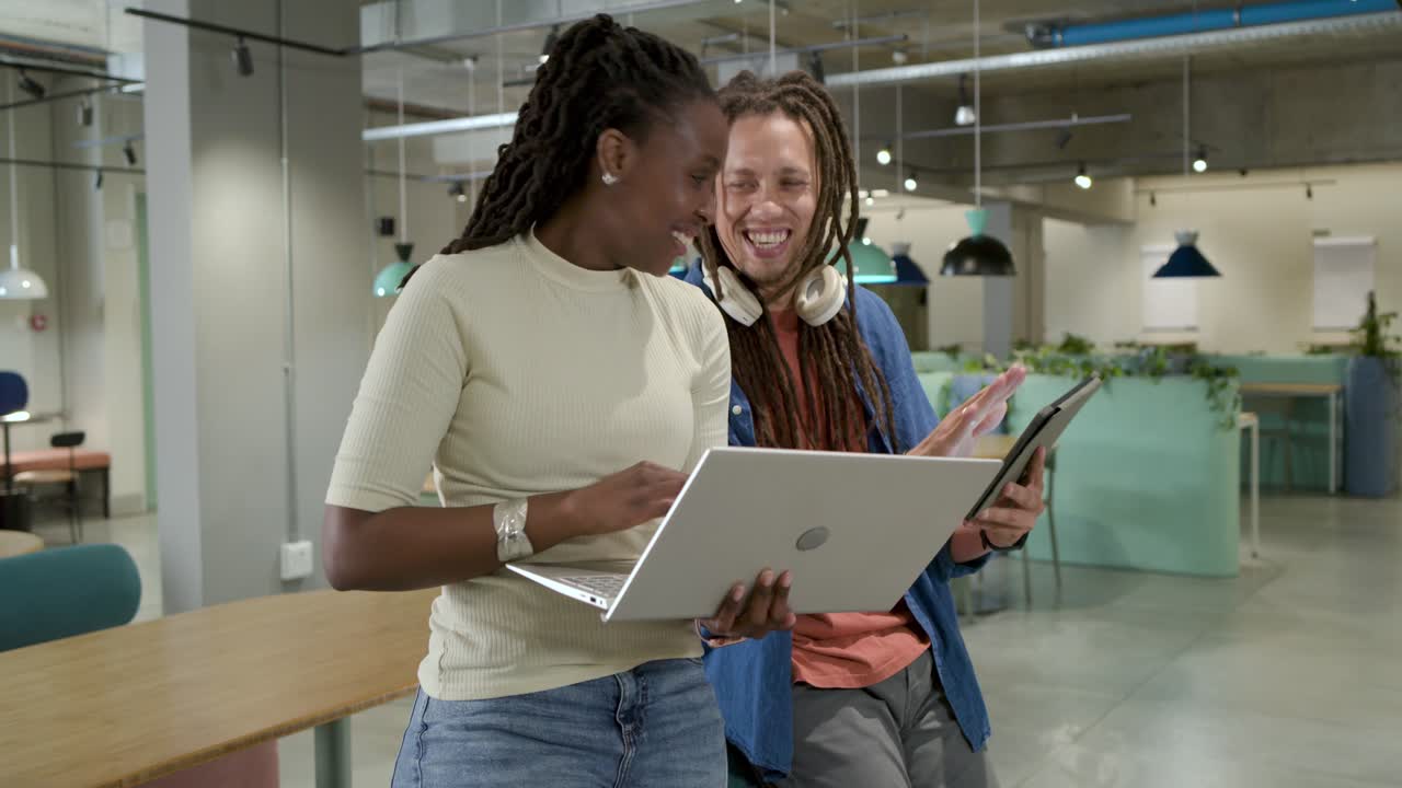 African American colleagues smiling while angling laptop tapping tablet agreeing in office lounge